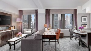 A hotel room with a dining area, a sofa, a TV, and large windows with a city view. - WestHouse Hotel New York, an SLH Hotel (New York)