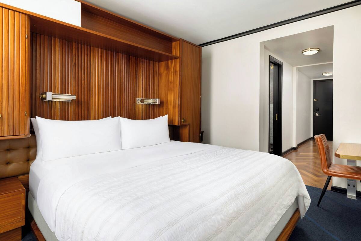Ein modernes Hotelzimmer mit einem großen Bett, Holzvertäfelung an den Wänden, einem kleinen Tisch und einem Sessel.