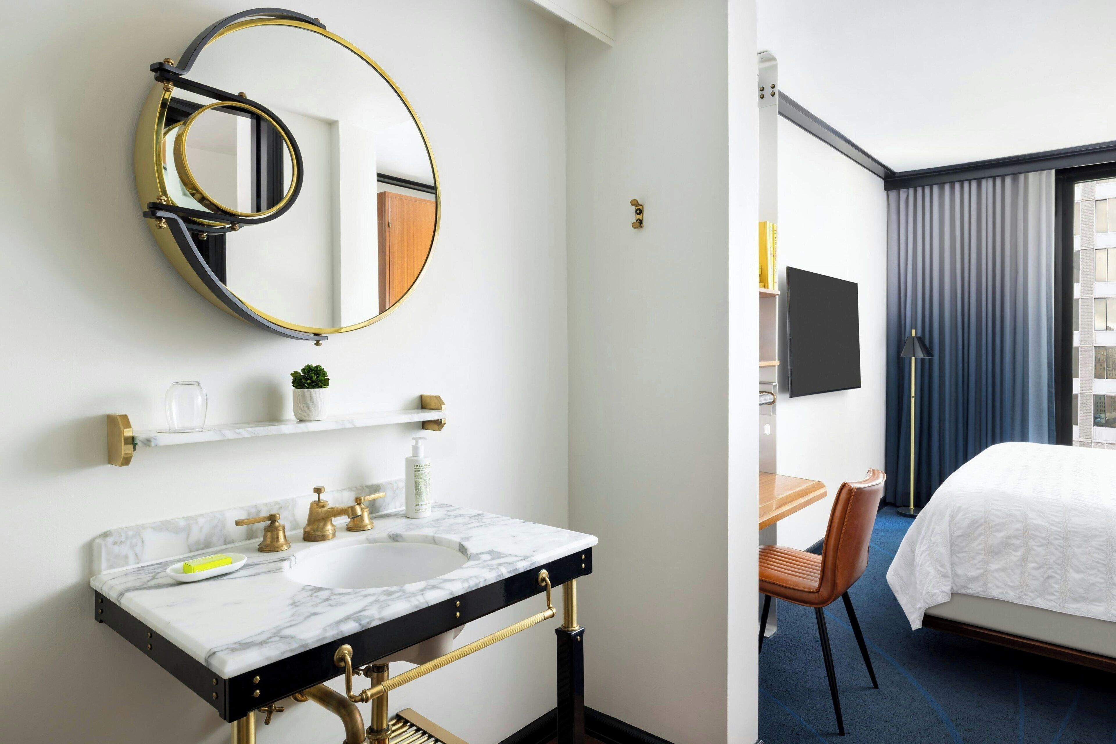 A hotel bathroom with a marble sink, gold fixtures, and a large mirror.