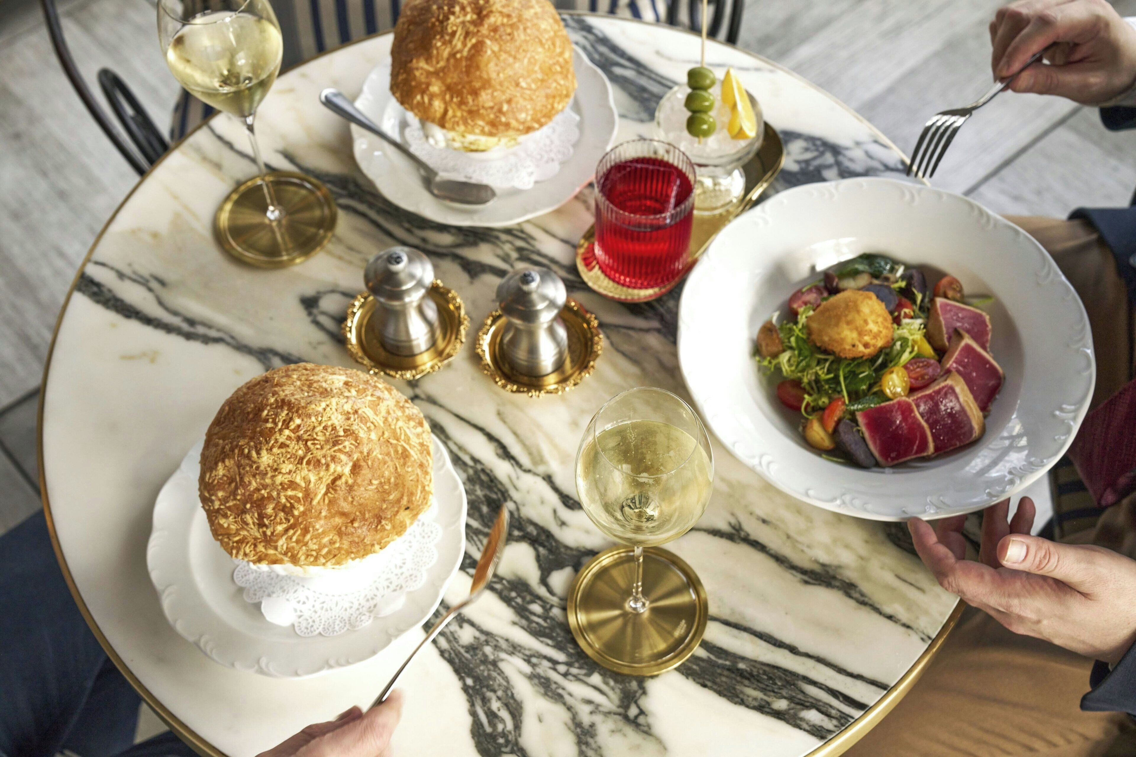 A marble table with a plate of food, a glass of wine, and a bread roll.