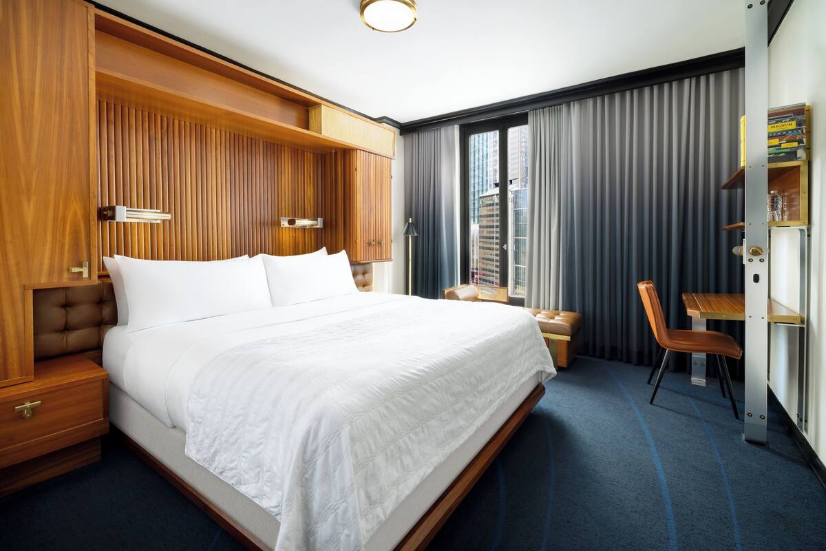 Ein modernes Hotelzimmer mit einem großen Bett, einem Holzkopfstück, einem Schreibtisch und einem Sessel.
