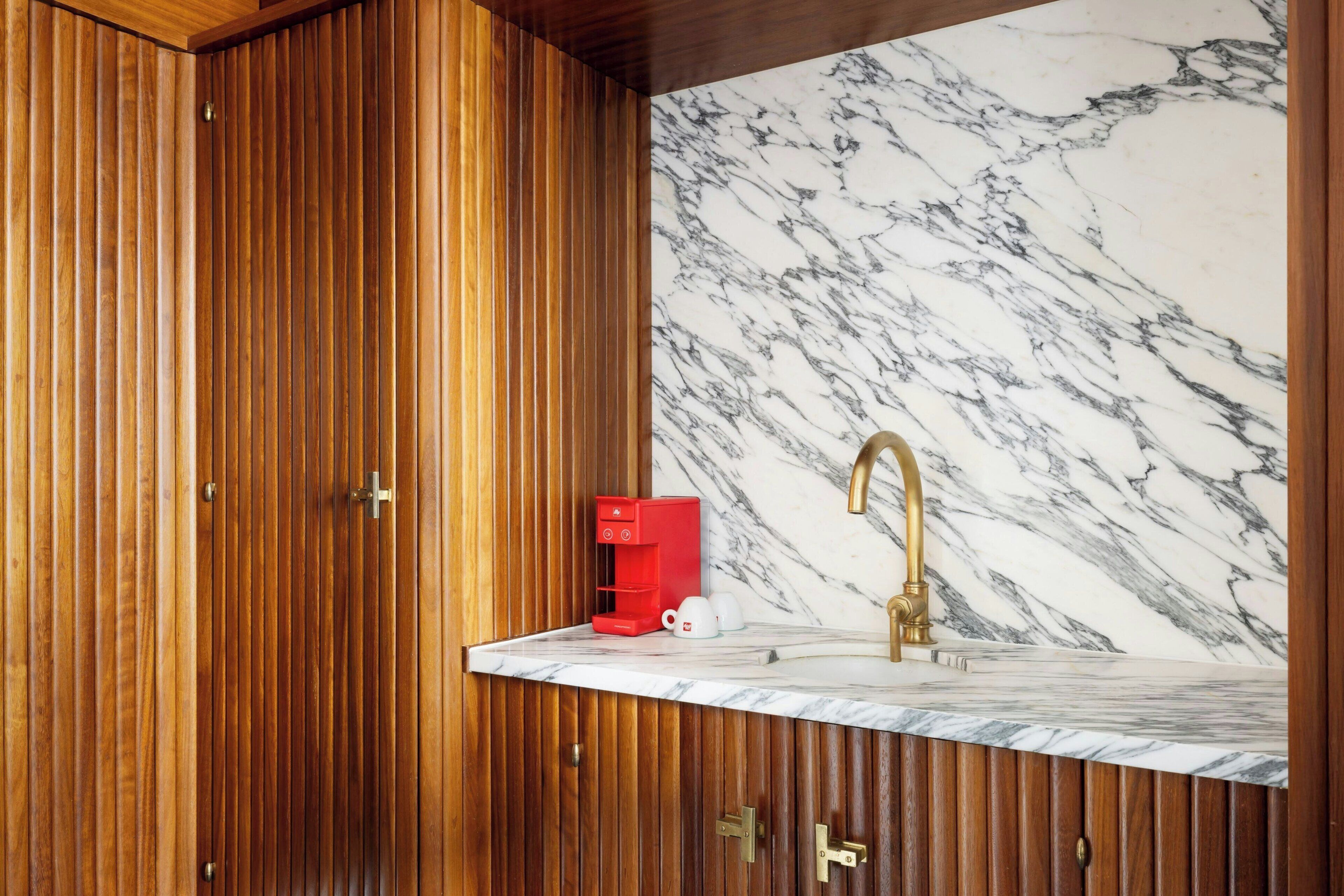 Una cucina con mobili in legno, una parete di fondo in marmo e un rubinetto dorato.