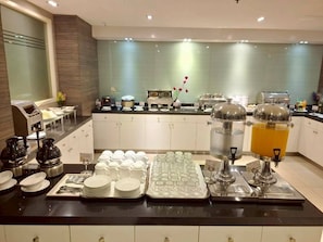 A hotel breakfast area with buffet setup, including plates, glasses, and a juice dispenser. - Crystal Suites Suvarnabhumi Airport (Bangkok)