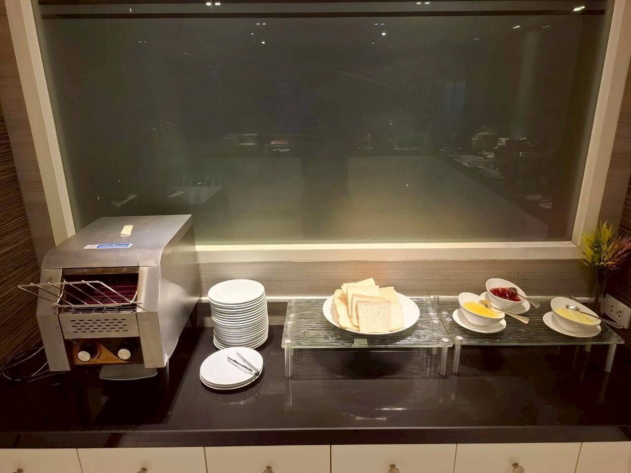 Un área de cocina con una sandwichera, platos apilados y un bufé con diversas opciones de comida.