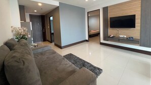 Una sala de estar moderna con un sofá, un televisor de pantalla plana montado en la pared y un pasillo que conduce a un dormitorio.