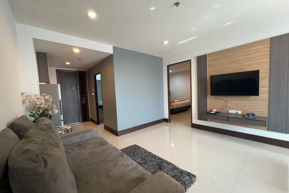 Una sala de estar moderna con un sofá, un televisor de pantalla plana montado en la pared y un pasillo que conduce a un dormitorio.