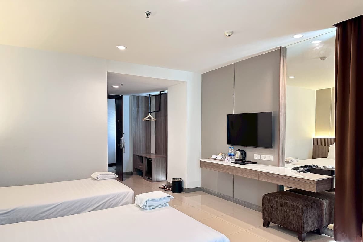 Habitación de hotel con dos camas, un televisor, un escritorio y un espejo grande.