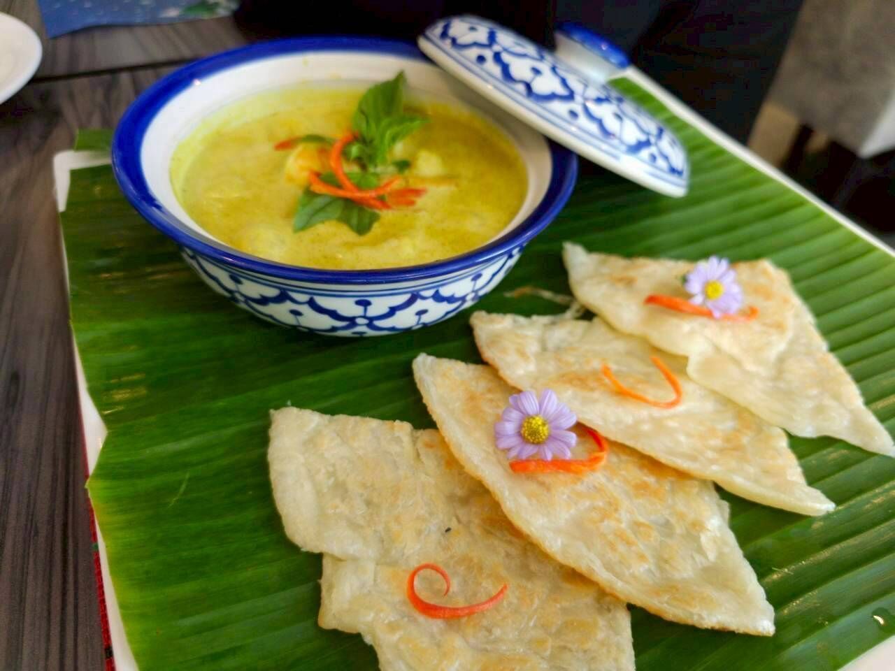 A bowl of soup with a blue and white pattern, accompanied by triangular flatbreads on a banana leaf.