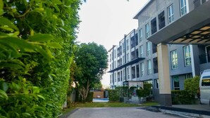 Un moderno edificio residencial de varios pisos con camino pavimentado y abundante vegetación.