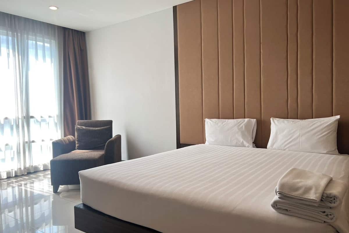 Una habitación de hotel con una cama grande, una silla y un ventanal con cortinas.