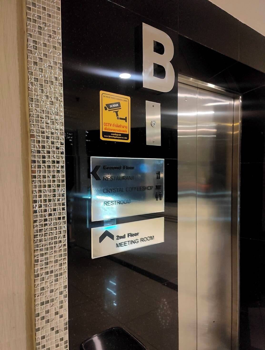 An elevator interior with a sign indicating CCTV surveillance, directional signs for the ground floor, and a sign for the second floor meeting room.