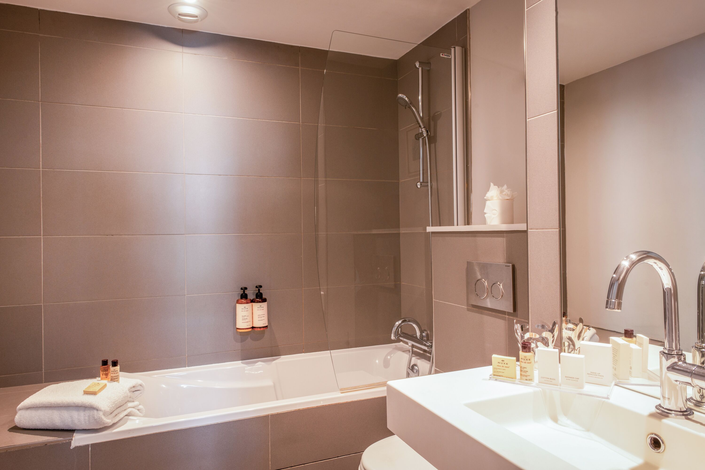 A modern bathroom with a bathtub, a sink, and a shower. There are toiletries on the sink and a towel on the bathtub.