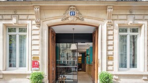 Entrada de un hotel con puerta de vidrio, un letrero con la letra 'H' y el número '49' sobre la puerta.