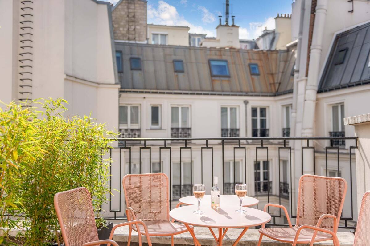 A balcony with a table and chairs, a bottle of champagne, and a view of buildings.