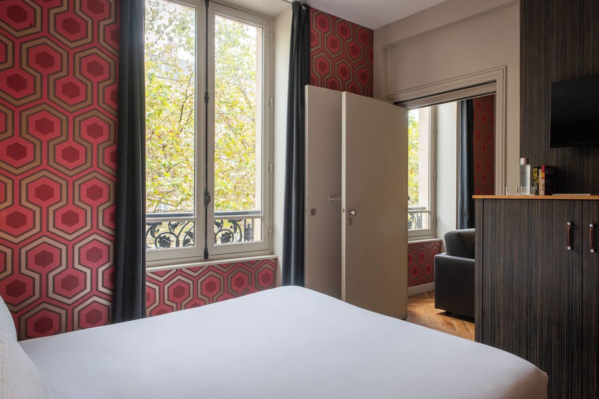 A bedroom with a large bed, a wardrobe, a television, and a window with a view of trees.