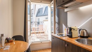 Cocina compacta con encimera de madera, un lavabo y ventana con vistas a un balcón con mobiliario exterior.