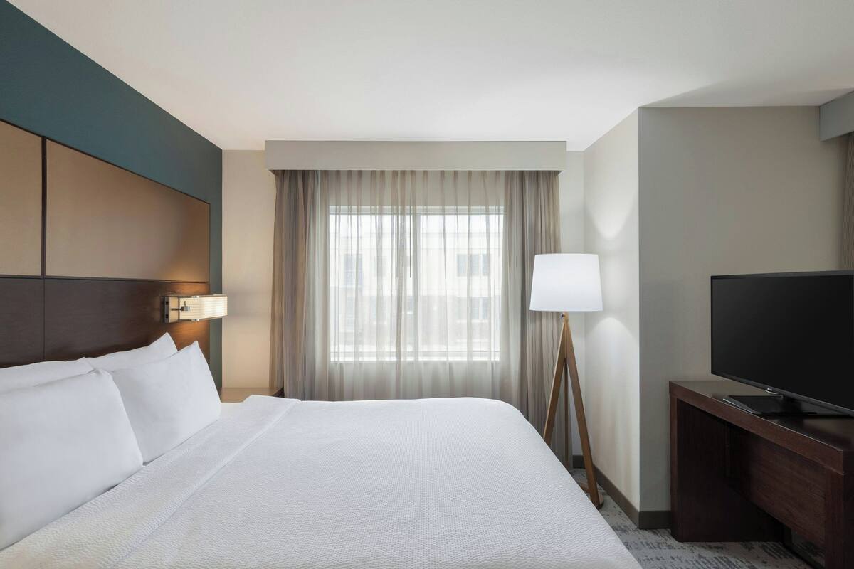 A hotel room with a large bed, a TV, a desk, and a window with curtains.