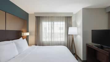 Una habitación de hotel con una cama grande, televisión, escritorio y ventana con cortinas.