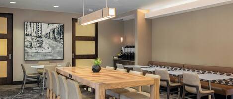 A hotel dining area with a large wooden table, multiple seating arrangements, and a large black-and-white cityscape painting on the wall.