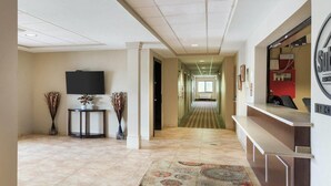 A hotel lobby with a reception desk, a flat-screen TV, a patterned rug, and a hallway leading to a room with a window. - Suburban Studios Triadelphia - Wheeling at The Highlands (Triadelphia)