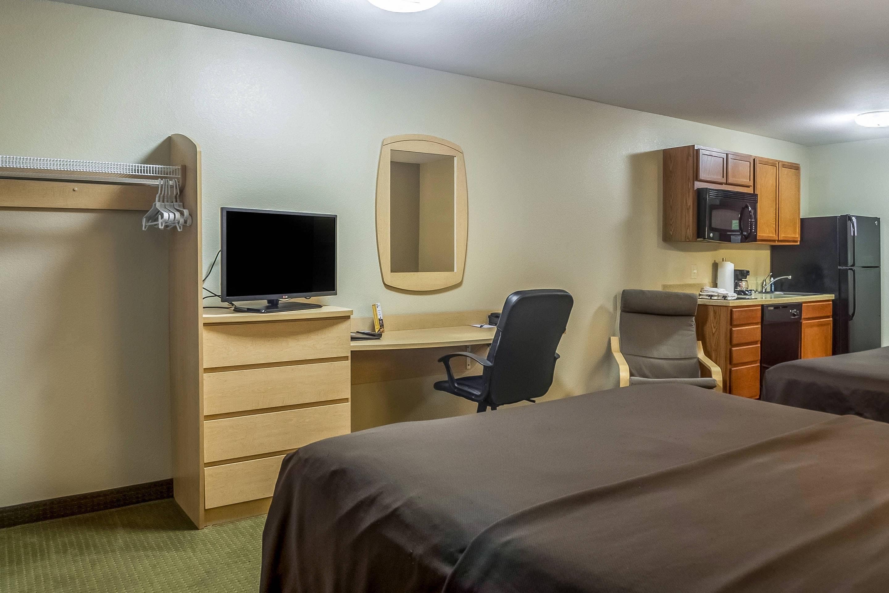 A hotel room with a desk, a television, a microwave, a refrigerator, and two beds.