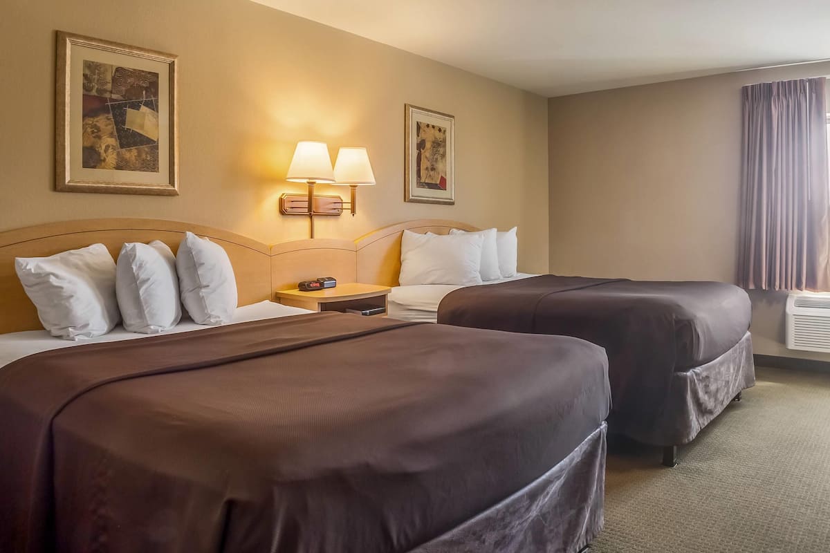 A hotel room with two beds, a nightstand, wall-mounted lamps, and framed artwork.