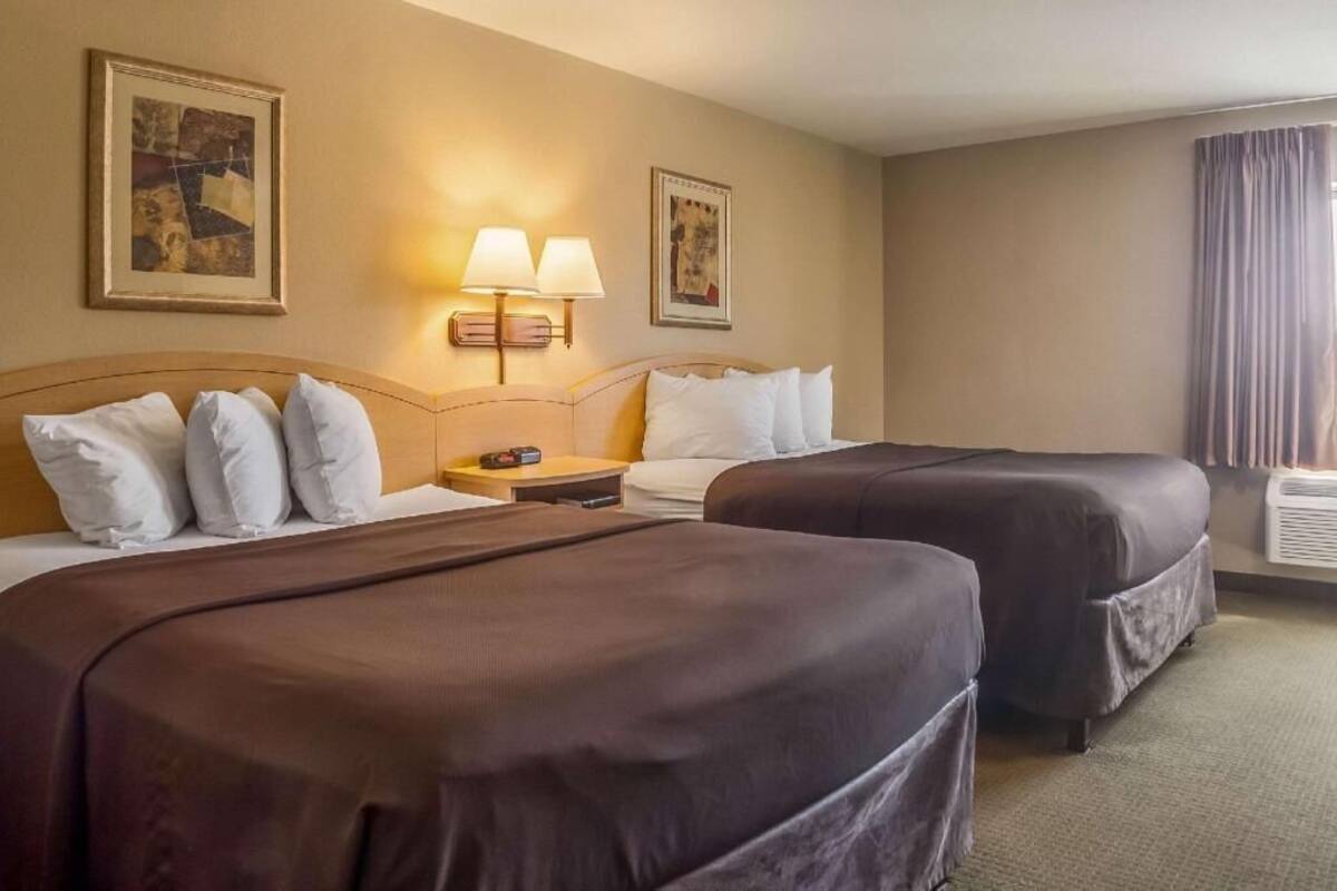 A hotel room with two beds, a nightstand, wall-mounted lamps, and a window with curtains.