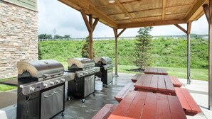 An outdoor patio with a stone wall, a wooden pergola, and a grill station. - Suburban Studios Triadelphia - Wheeling at The Highlands (Triadelphia)