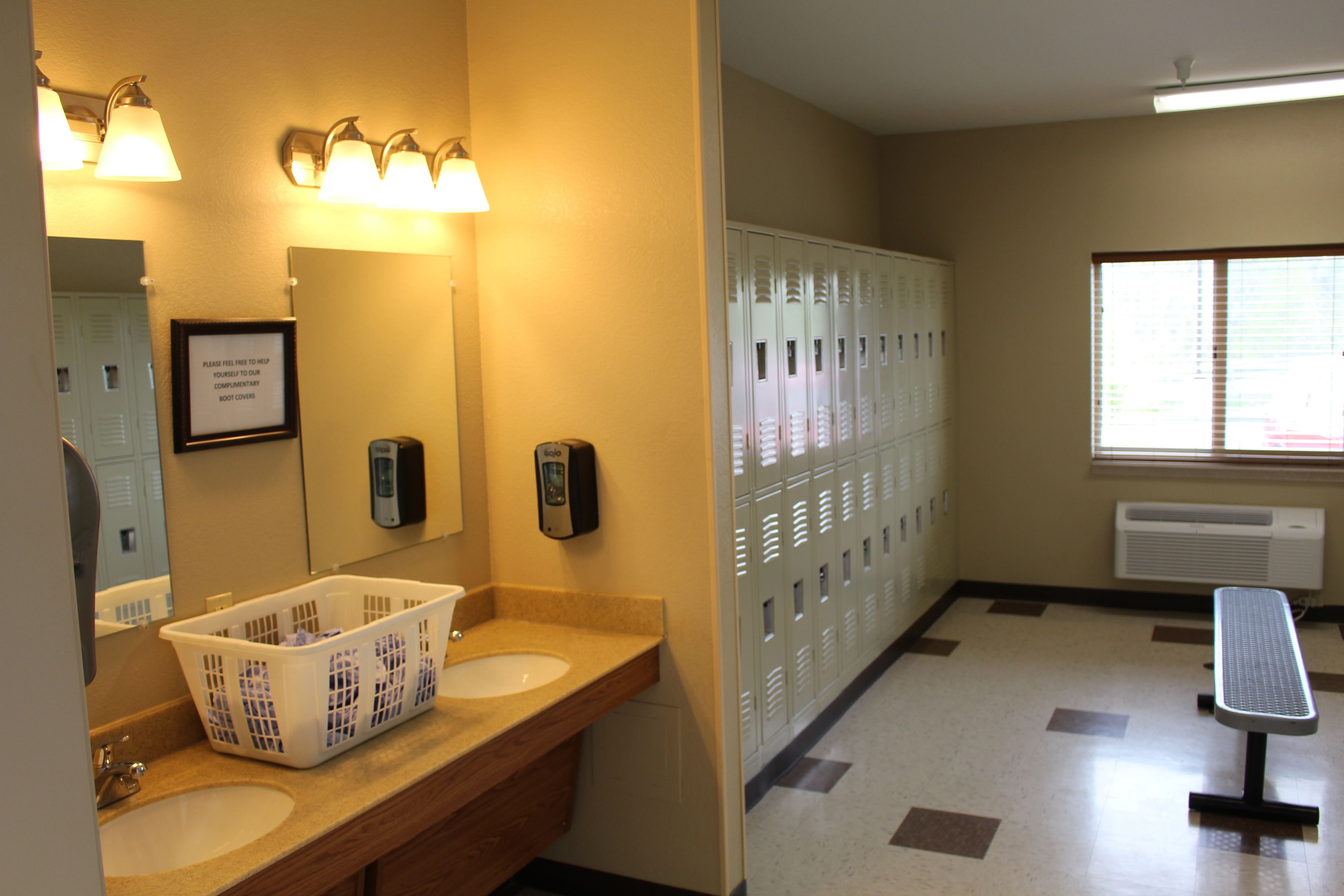 A bathroom with two sinks, a mirror, a hand dryer, a trash can, and a bench.