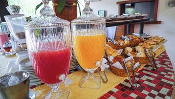A buffet table with two large glass containers, one with a red beverage and the other with a yellow beverage, and a variety of bread and pastries.