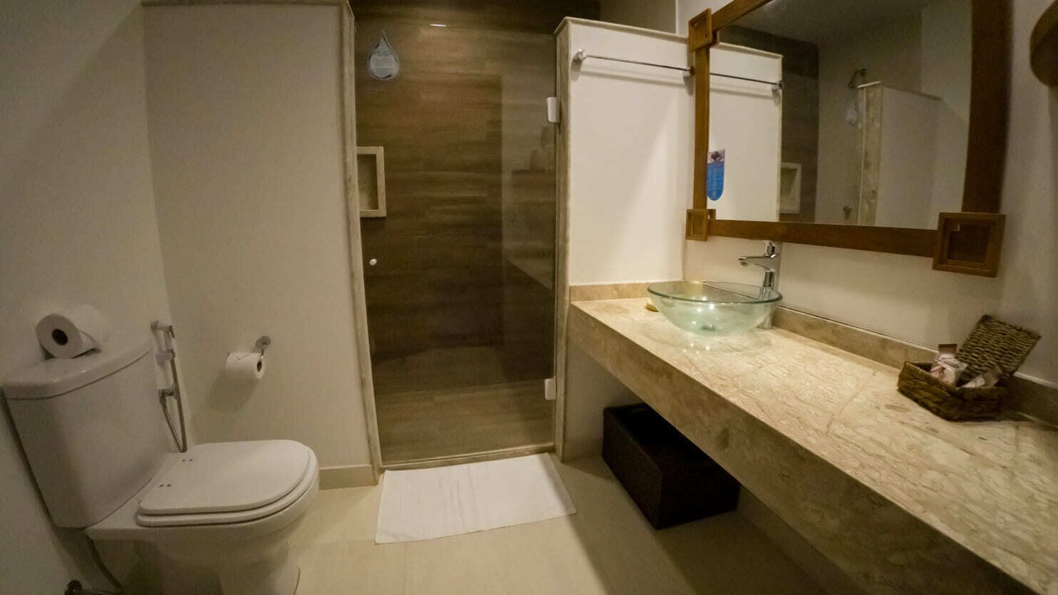 A bathroom with a toilet, a glass sink, a mirror, and a shower.