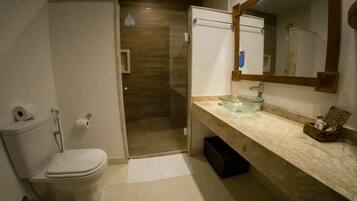 A bathroom with a toilet, a glass sink, a mirror, and a shower.