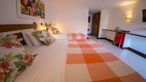 A hotel room with a bed, floral bedspread, a checkered rug, a painting on the wall, and a kitchenette area. - Azeda Boutique Hotel João Fernandes (Búzios)