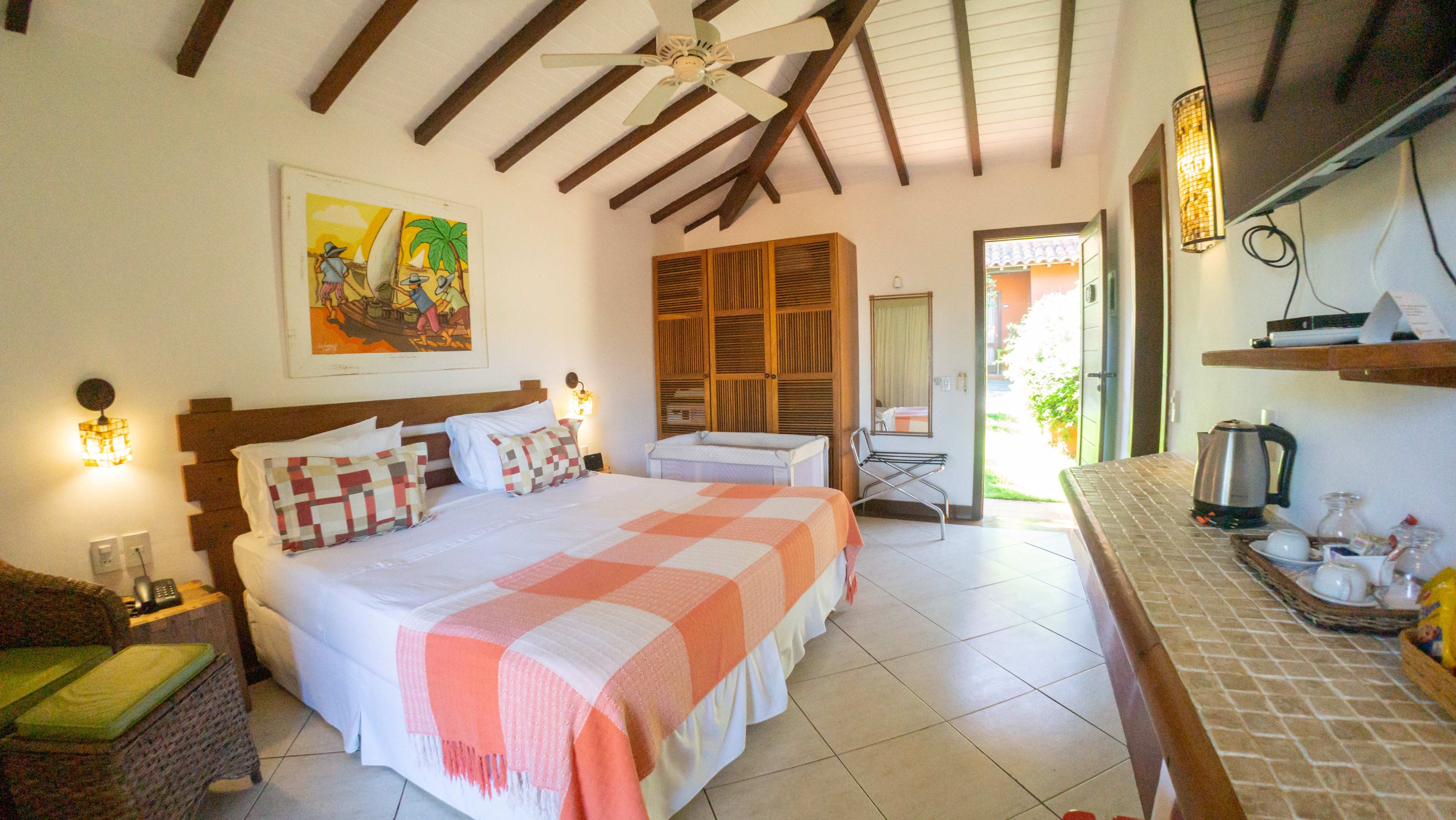 Ein Hotelzimmer mit einem großen Bett, einem Holz-Kopfteil, einem Bild an der Wand, einem kleinen Tisch mit Wasserkocher und Blick ins Freie.