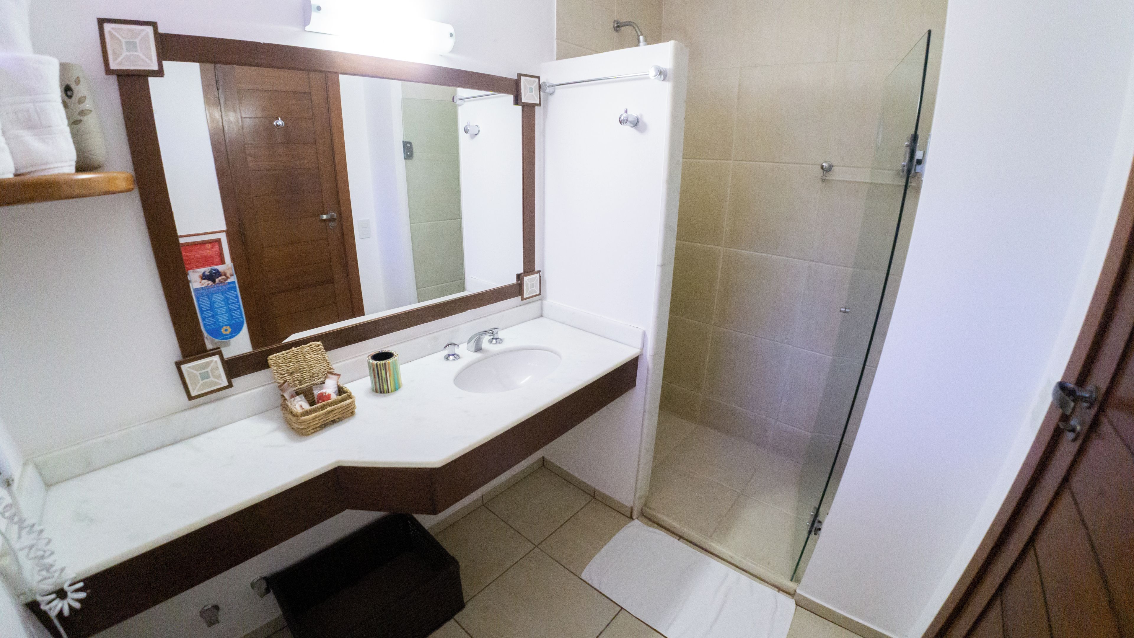 Un baño con lavamanos blanco, un espejo, ducha y toallero.