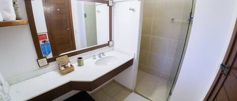 Un baño con lavamanos blanco, un espejo, ducha y toallero.