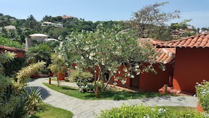 A pathway leading to a building with a red facade, surrounded by greenery and a clear sky. - Azeda Boutique Hotel João Fernandes (Búzios)