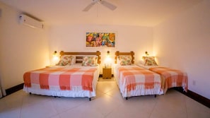A hotel room with two beds, each with a checkered blanket, a ceiling fan, a painting on the wall, and a nightstand with a lamp. - Azeda Boutique Hotel João Fernandes (Búzios)