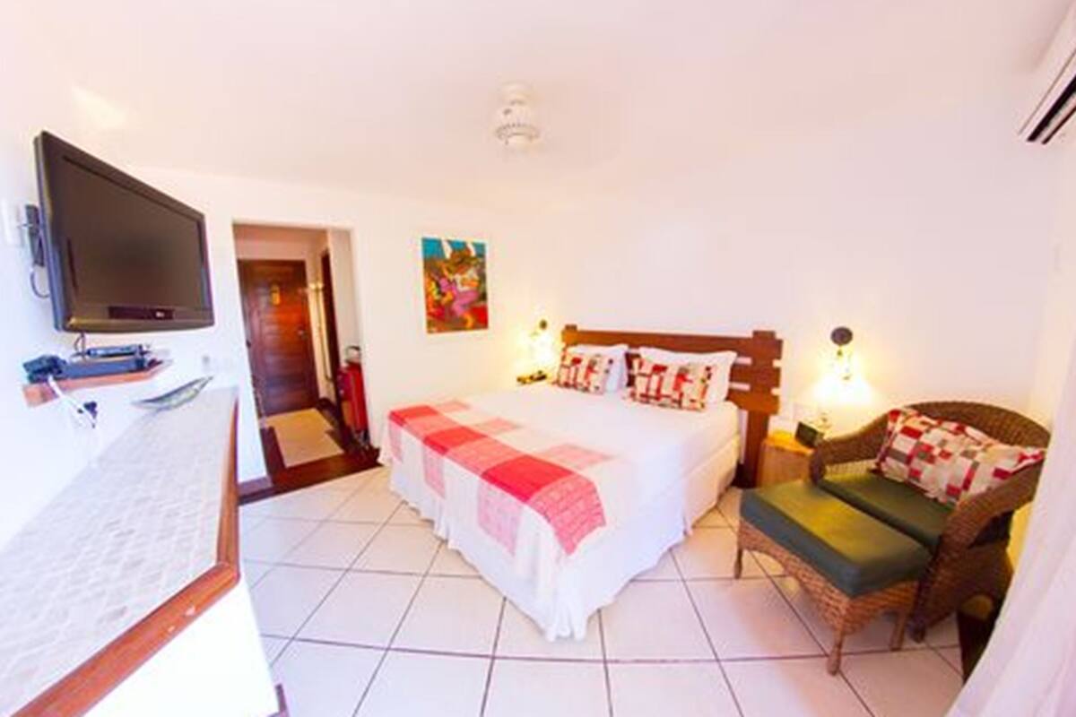 A hotel room with a bed, a television, a chair, and a painting on the wall.