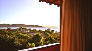 A view from a balcony with a red roof, overlooking a coastal area with hills and a body of water.