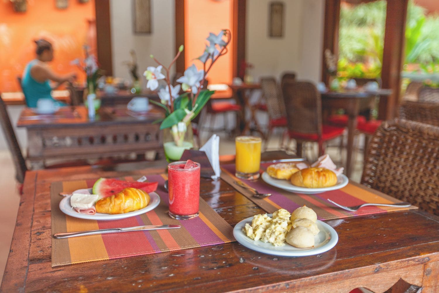 A breakfast setting with croissants, scrambled eggs, and a fruit drink on a wooden table.