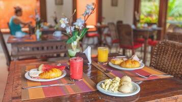 A breakfast setting with croissants, scrambled eggs, and a fruit drink on a wooden table.