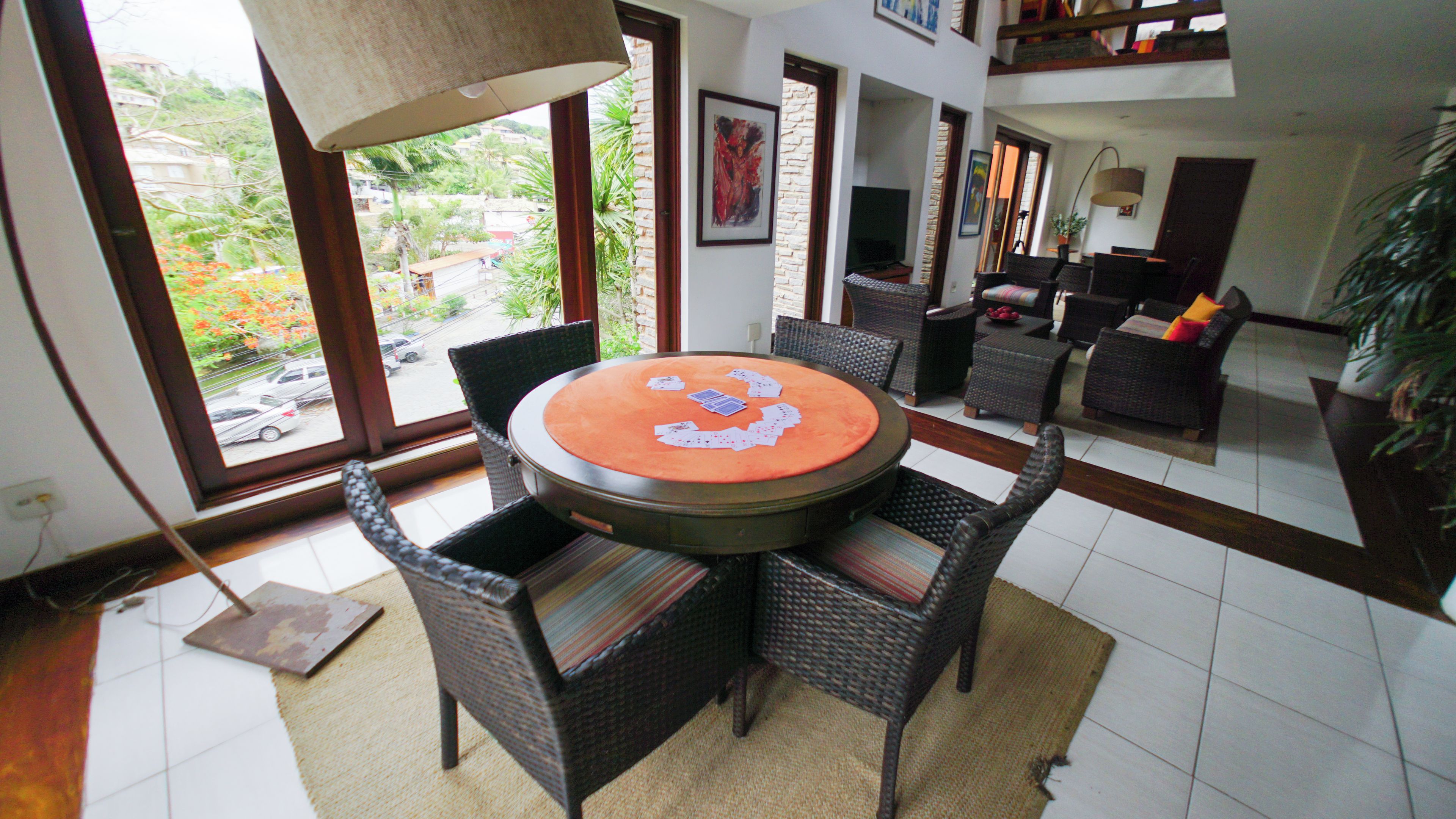 A dining area with a round table, wicker chairs, and a view of the outdoors through large windows.