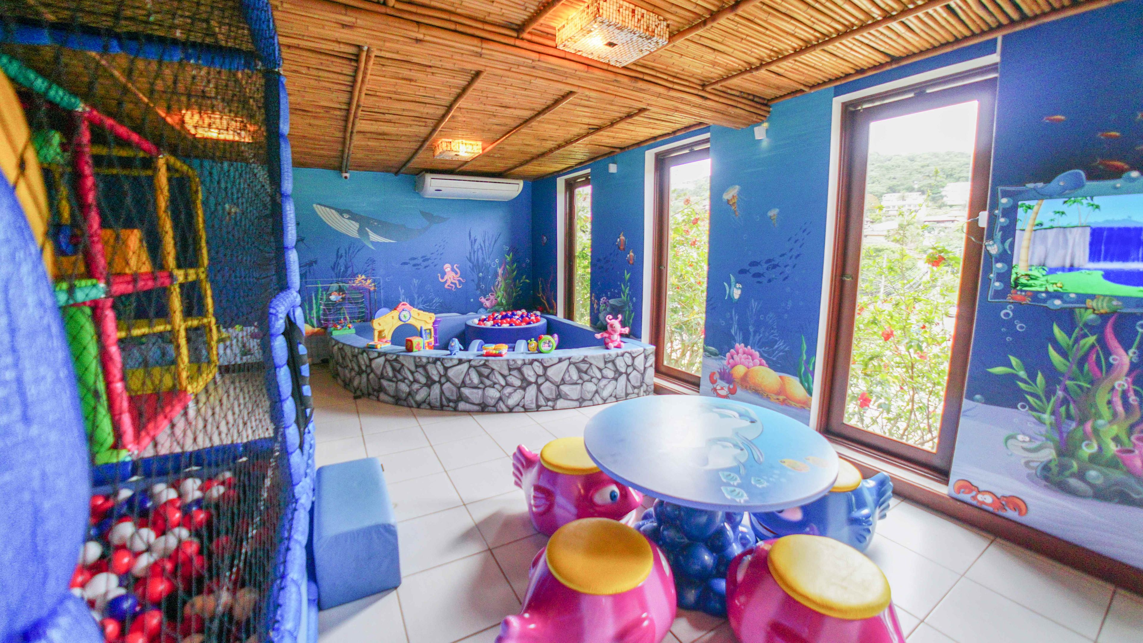 Área de recreação infantil com mesa de bilhar, assentos e uma janela grande com um mural subaquático.
