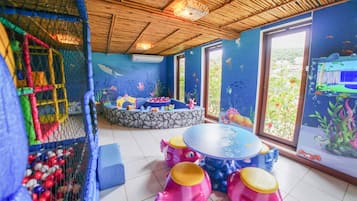 Área de recreação infantil com mesa de bilhar, assentos e uma janela grande com um mural subaquático.