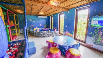 Spielbereich für Kinder mit Billardtisch, Sitzgelegenheiten und einem großen Fenster mit Unterwassermalerei.