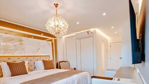 A modern hotel room with a large bed, a chandelier, a flat-screen TV, and a minibar.