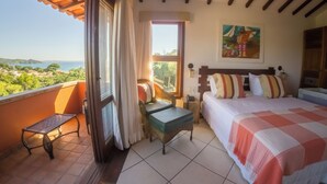 A bedroom with a bed, a small table, a bench, and a view of the sea.