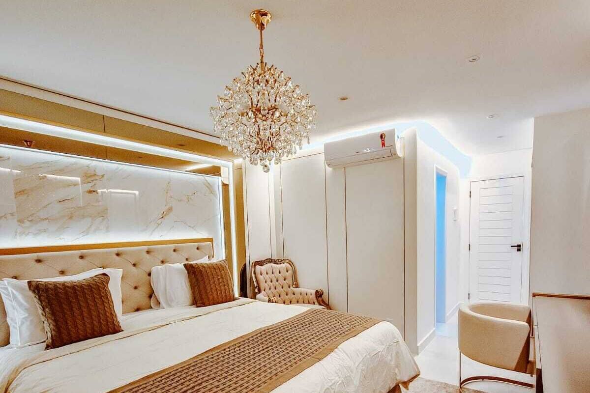 A modern bedroom with a large bed, a chandelier, and a view of the hallway.