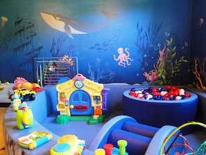 Zona de juegos infantiles con temática submarina en azul, que incluye una casita en forma de submarino y una piscina de pelotas.
